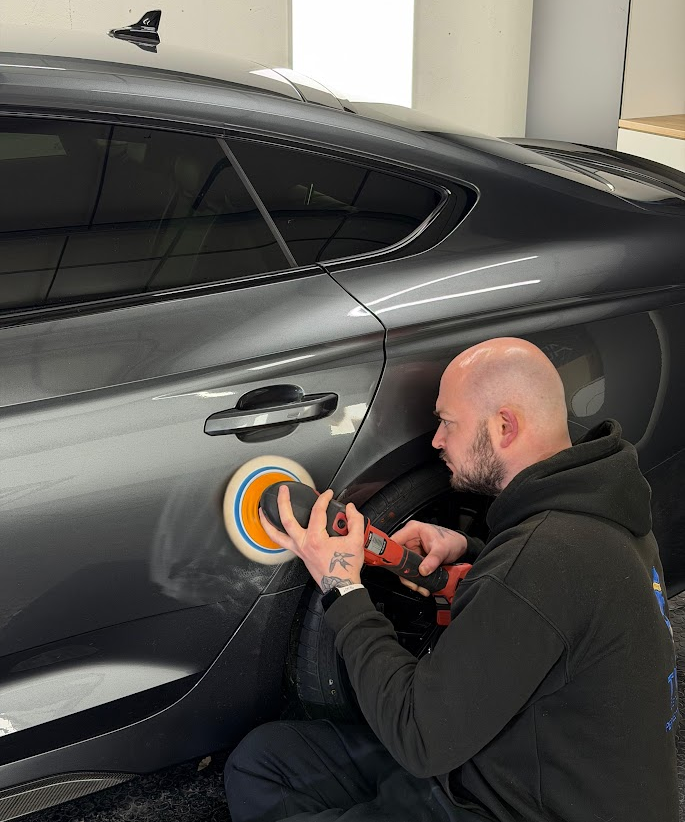 Jordan machine polishing a grey sports car in his detailing unit